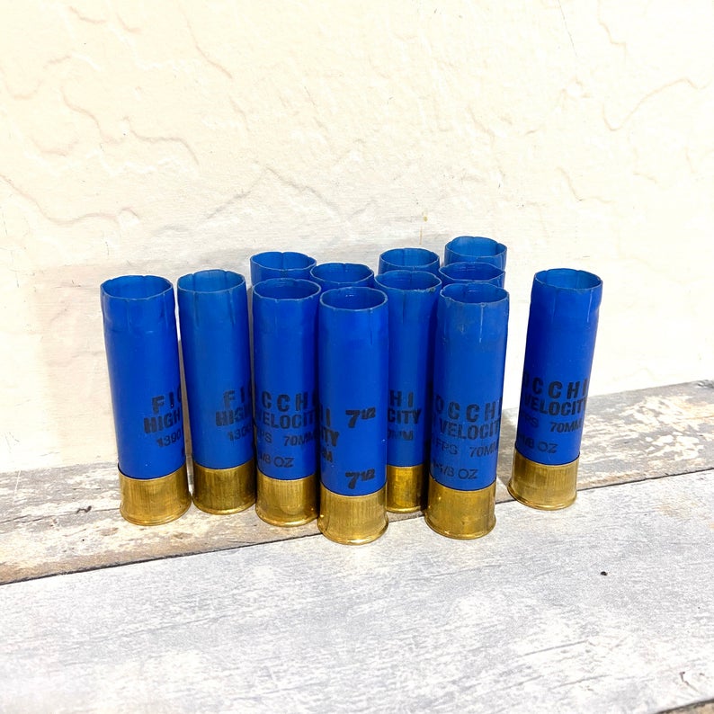 9 blue Fiocchi 16 gauge shotgun shells standing upright against a white wall