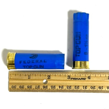 Two blue emmpty shotgun shells placed next to a wooden ruler for measurement.