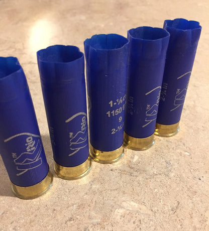 Five blue Rio 12 gauge shotgun hulls standing upright showing printed specifications and open plastic top crimps.