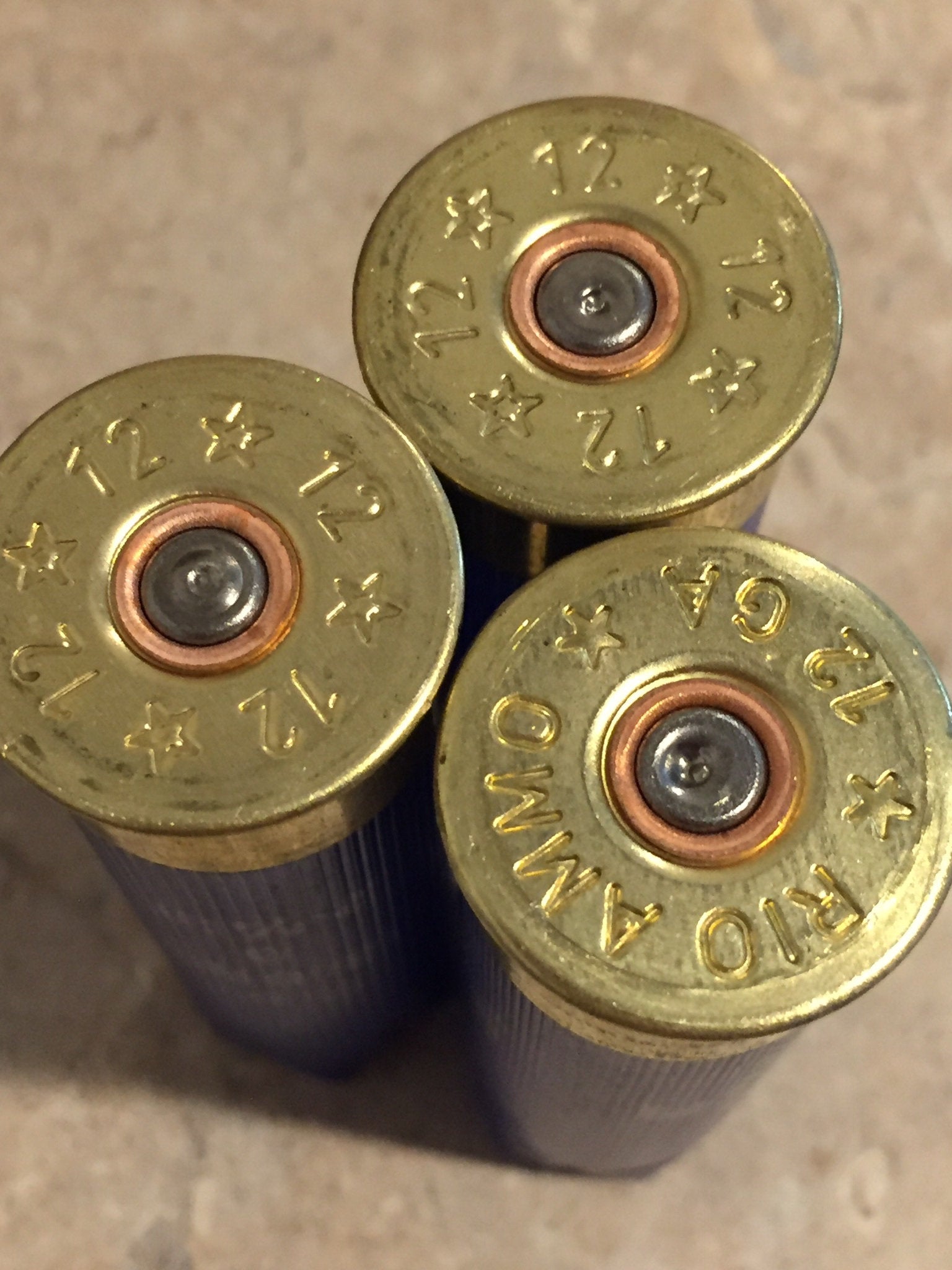 Macro view of three blue Rio 12 gauge shotgun shells standing upright showing stamped brass bases and spent primers.