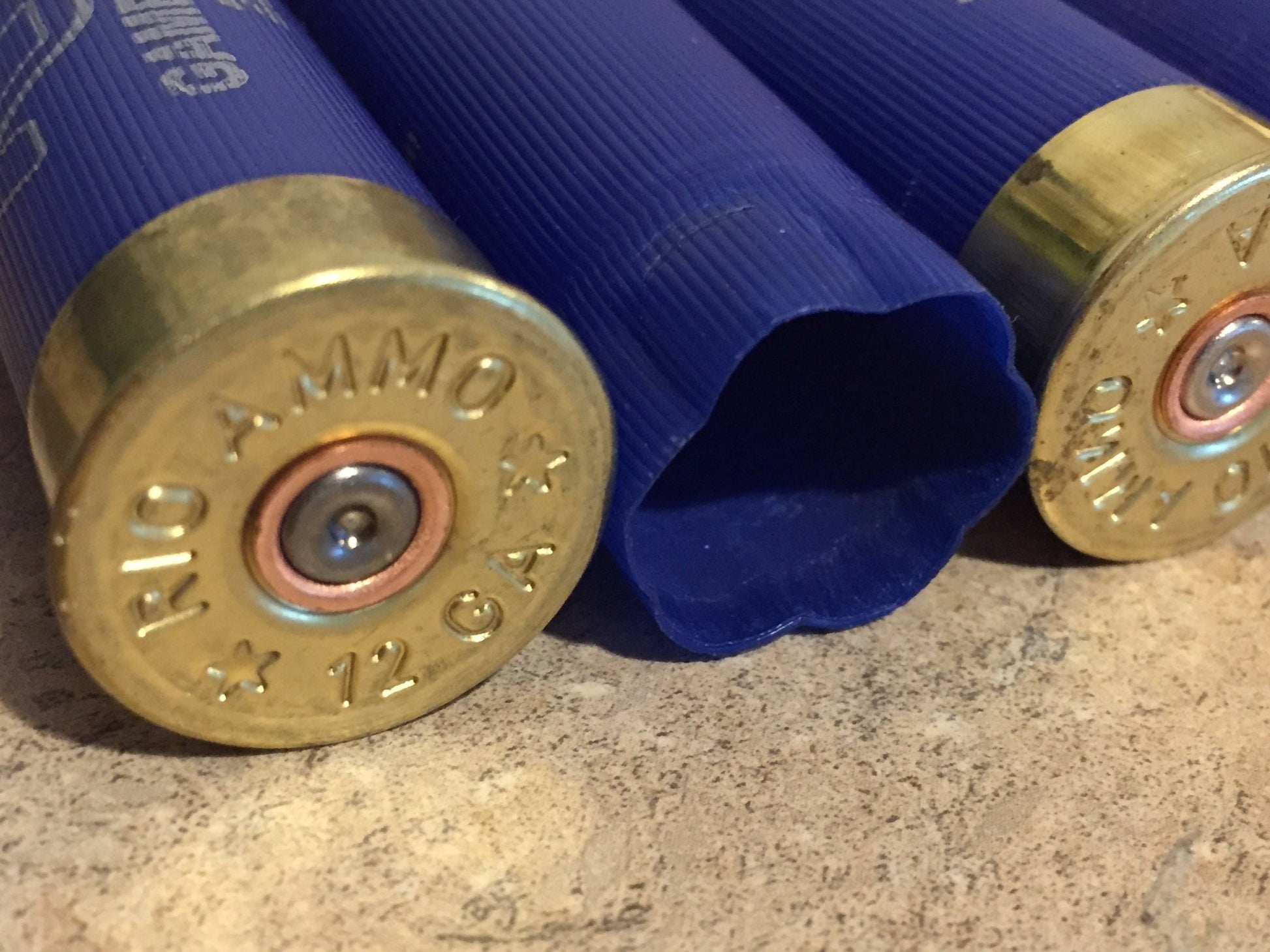 Macro view of three blue Rio 12 gauge shotgun shells standing upright showing stamped brass bases and spent primers.
