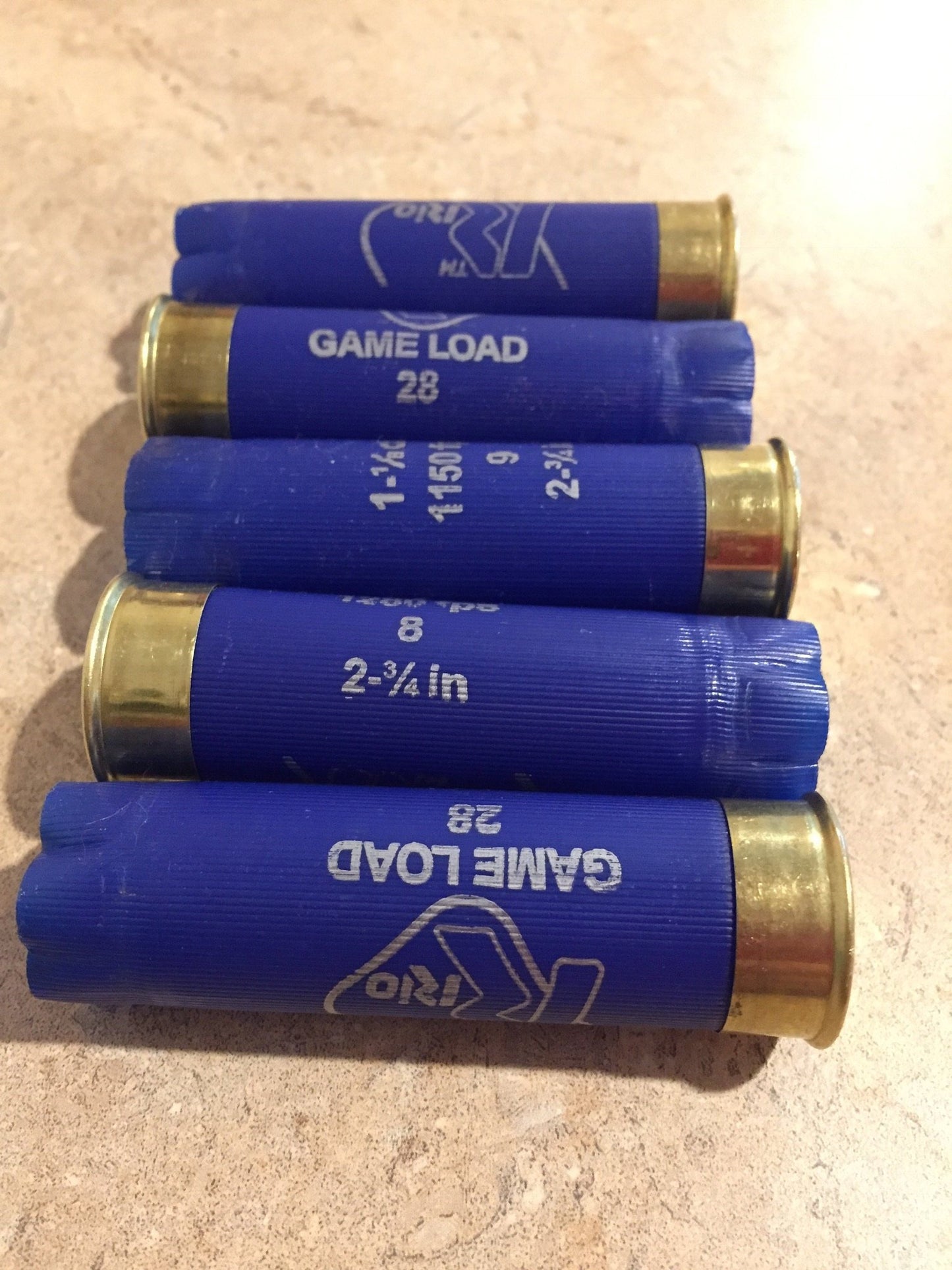 Five blue Rio 12 gauge shotshells stacked horizontally in alternating directions on a tan countertop.