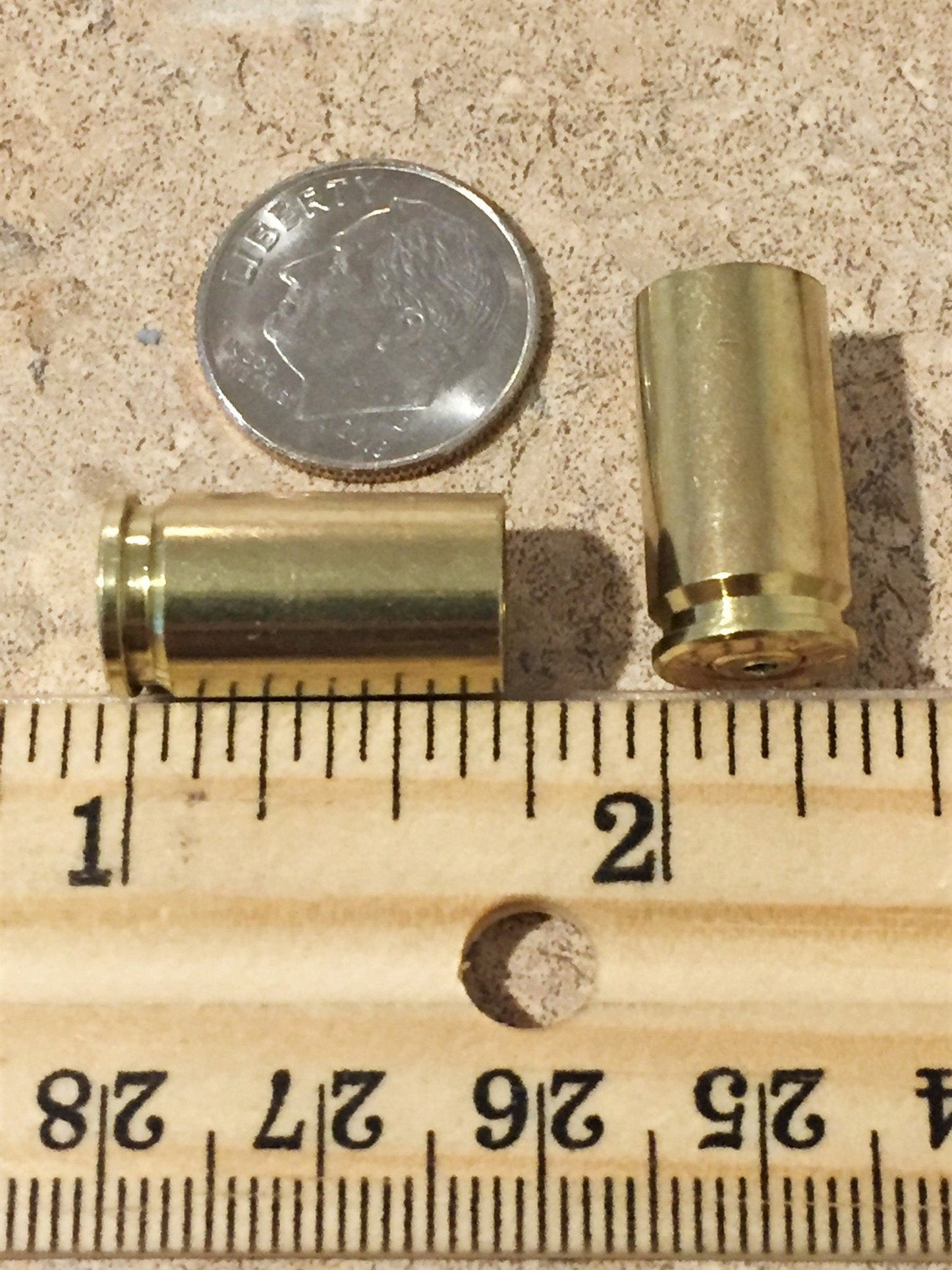 Two empty brass 9mm casings shown beside a dime and a wooden ruler for size comparison.