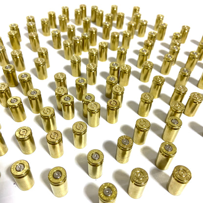 Once-fired brass 9mm casings standing upright in neat rows, with primers visible at their bases.
