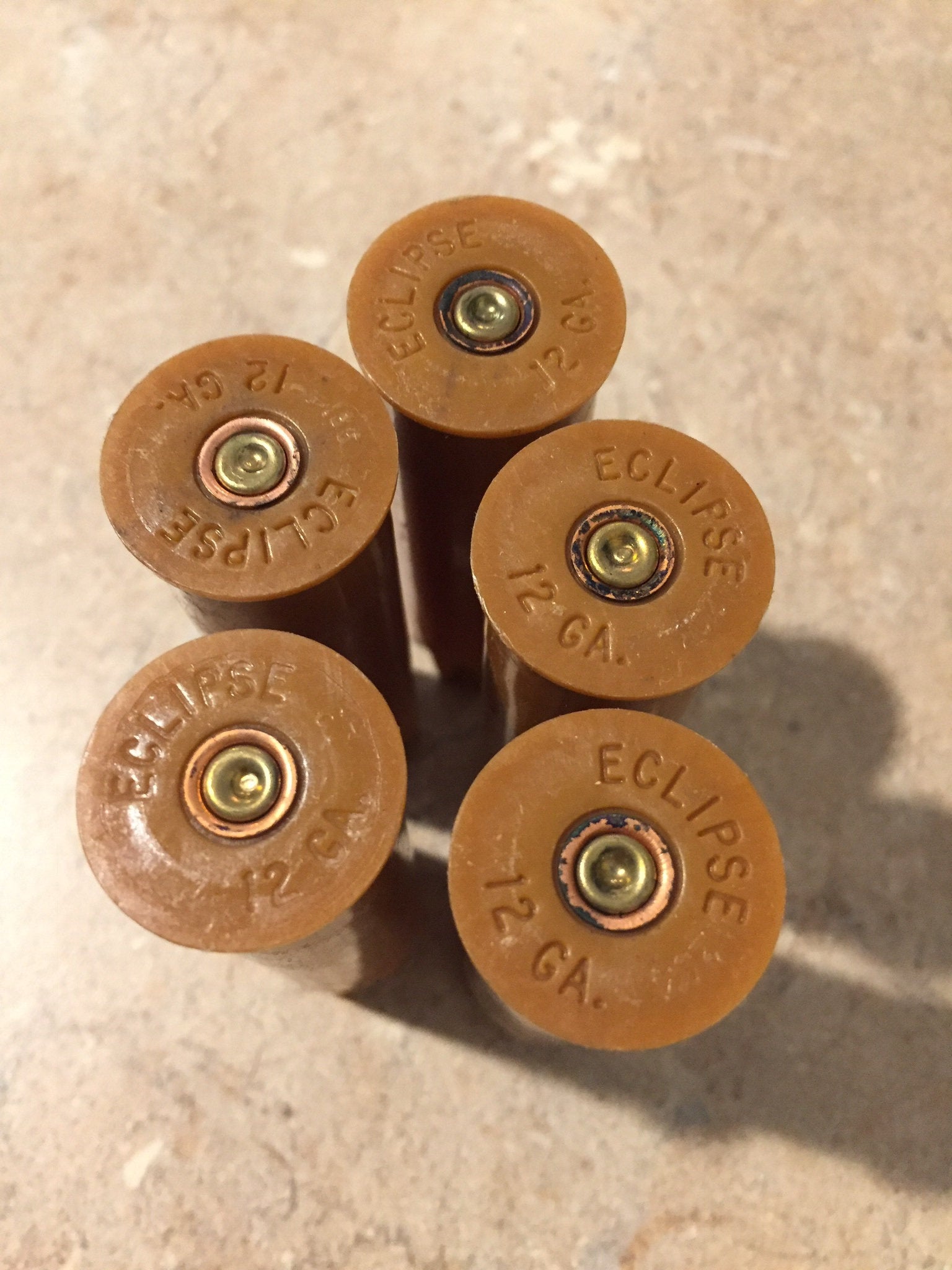 Five brown tan ‘Eclipse’ 12 gauge shotgun shell bases viewed from above, showing brass primers
