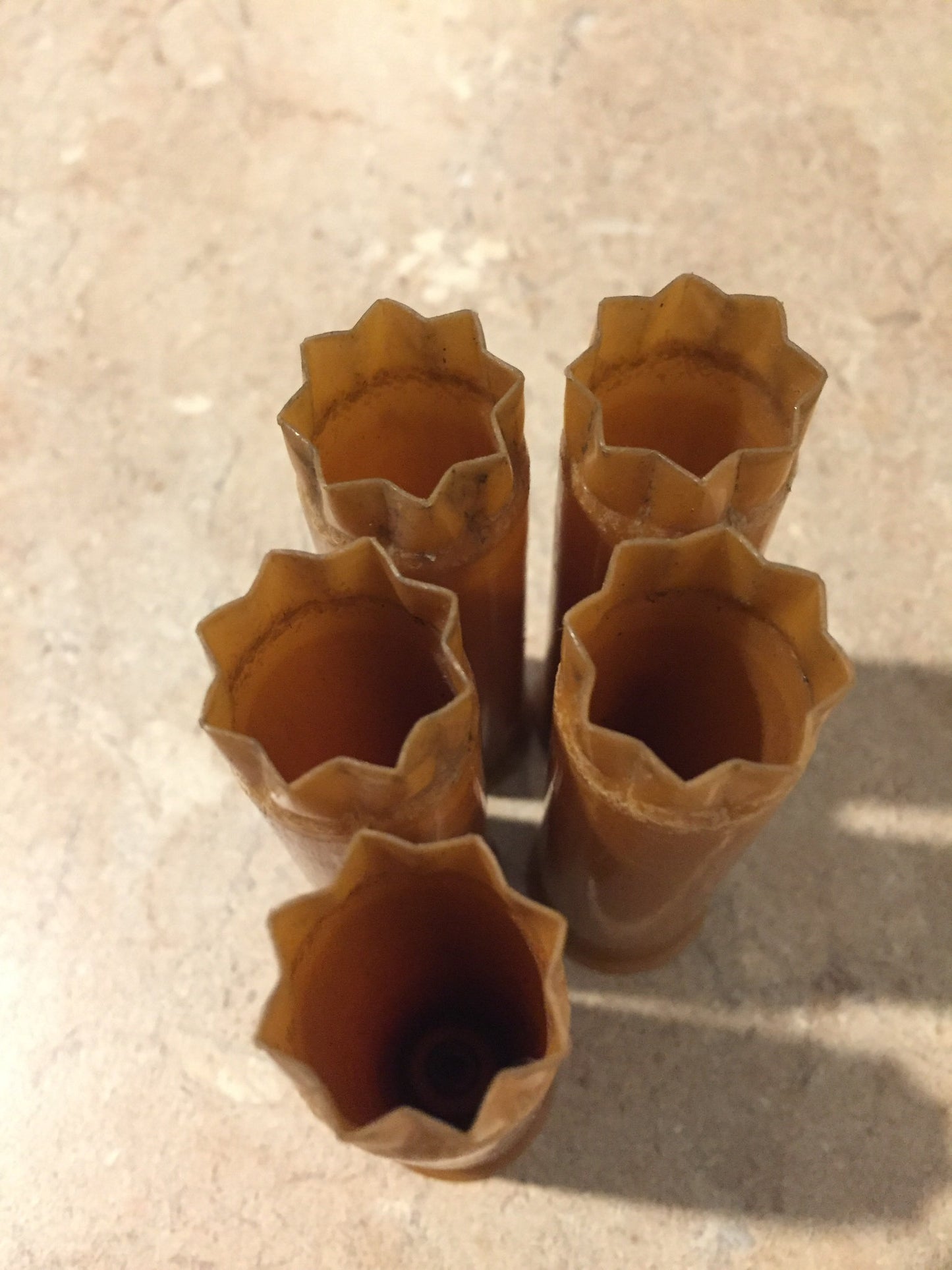 Five brown tan 12 gauge shotgun shells standing upright, viewed from the open star-crimped mouths