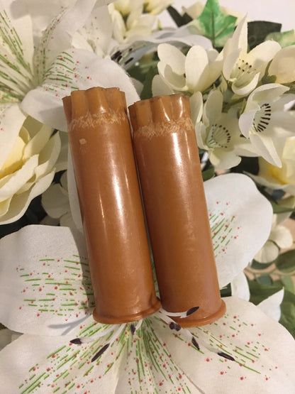 Two brown tan 12 gauge shotgun shells with worn star-crimped tops standing against a floral fabric background