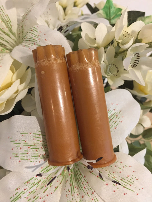 Two brown tan 12 gauge shotgun shells with worn star-crimped tops standing against a floral fabric background