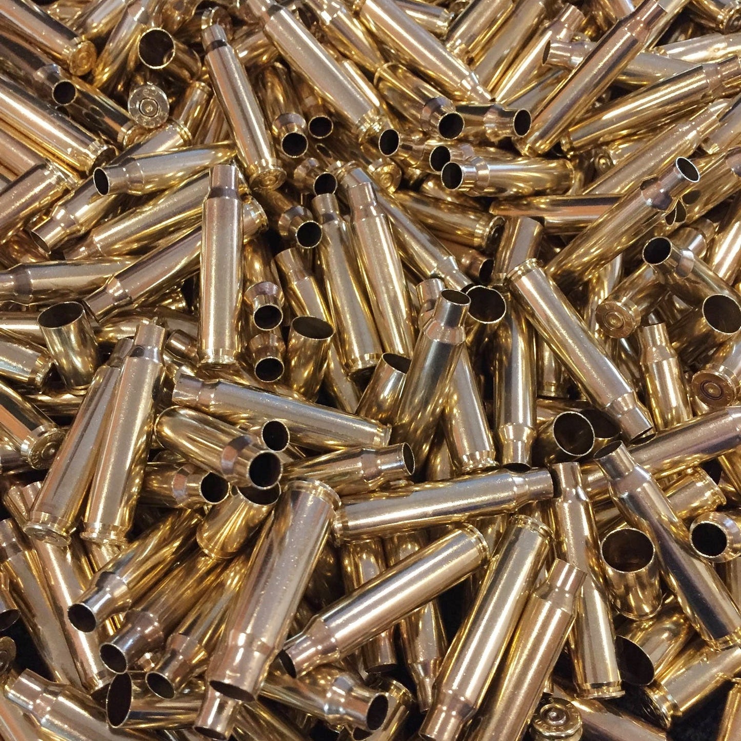 Frame-filling pile of bright yellow polished .223 brass cartridges showing open mouths and spent primer bases.
