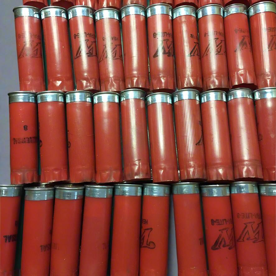 Close-up view of tightly packed, recovered red 12-gauge empty shotgun shells arranged side-by-side in dense horizontal rows. The ribbed plastic hulls feature silver-colored bases and various black printed text, including "UNIVERSAL", "WINCHESTER", and "EXTRA-LITE-8". The uniform layout showcases the clean, hand-inspected quality of the bulk lot.