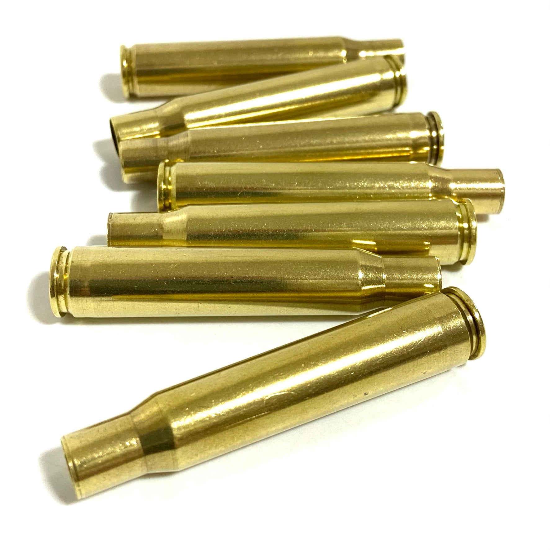 Seven polished bullet casings stacked horizontally on a plain white background, with one casing angled in front.
