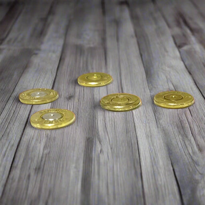 Five thin brass bullet slices scattered on a weathered wood plank, showing thin edge profiles