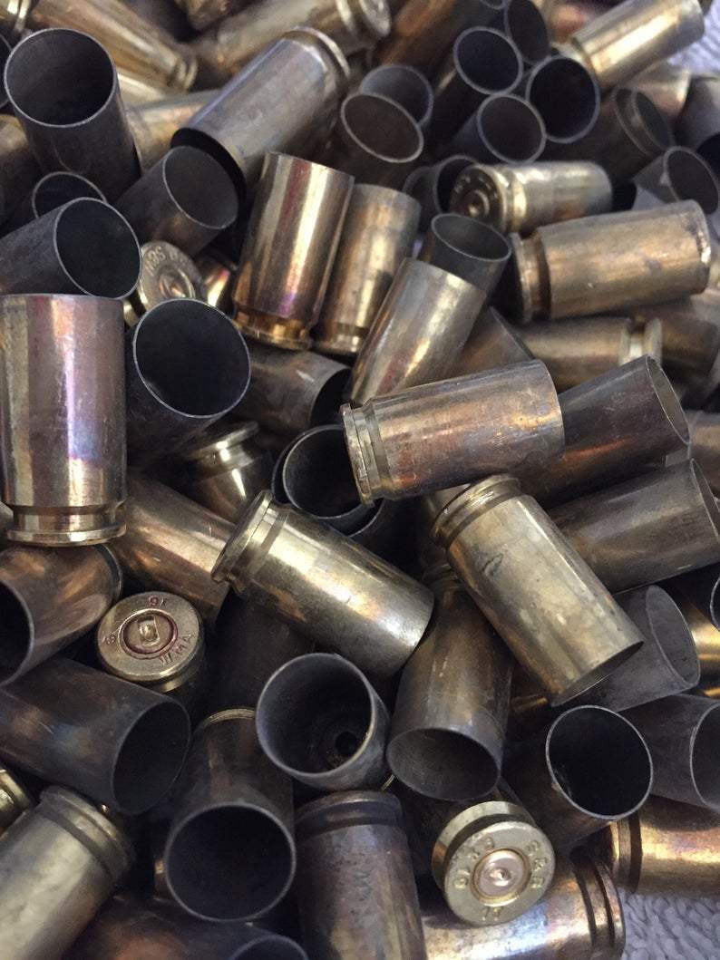 Dense jumbled pile of brass casings, some with a rainbow heat-tarnished finish