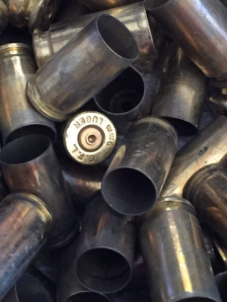 Jumbled pile of dark, tarnished brass casings with one headstamp reading 9MM LUGER visible