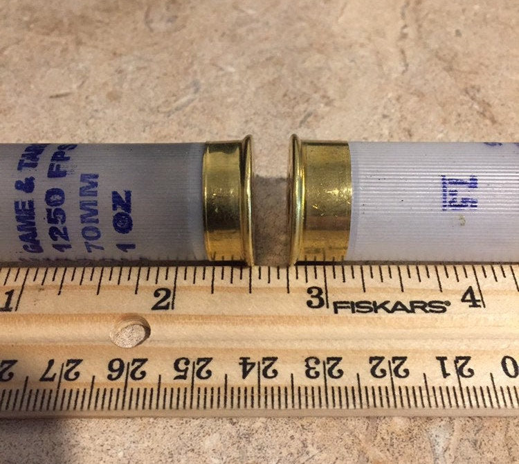 Two translucent white Fiocchi 12 gauge shotgun shells lying next to a wooden ruler showing their length