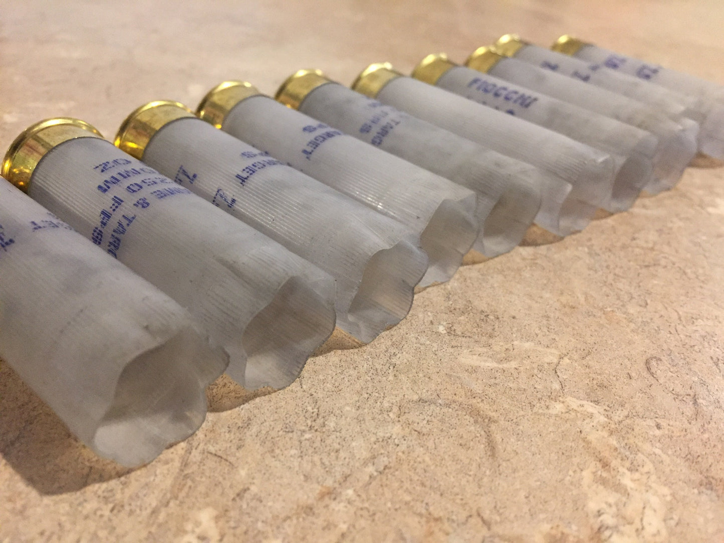 10 translucent white Fiocchi 12 gauge shotgun shells lying in a row viewed from the open mouth end