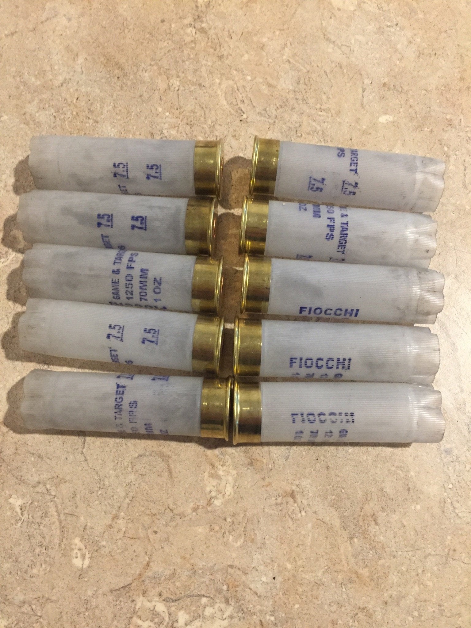 10 translucent white Fiocchi 12 gauge shotgun shells lying in a row with brass heads and open mouths