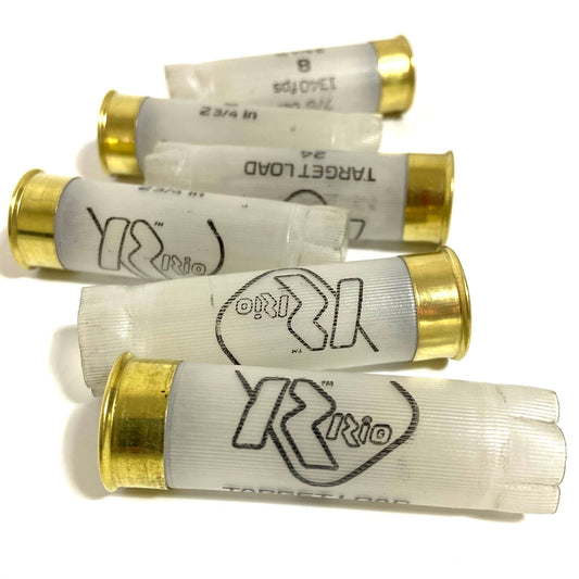 Four translucent Rio 12 gauge empty shotgun hulls with gold metal bases lying horizontally against a white background.
