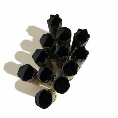 Cluster of black shotgun shells viewed from above, showing their crimped star-shaped tops on a wood surface.