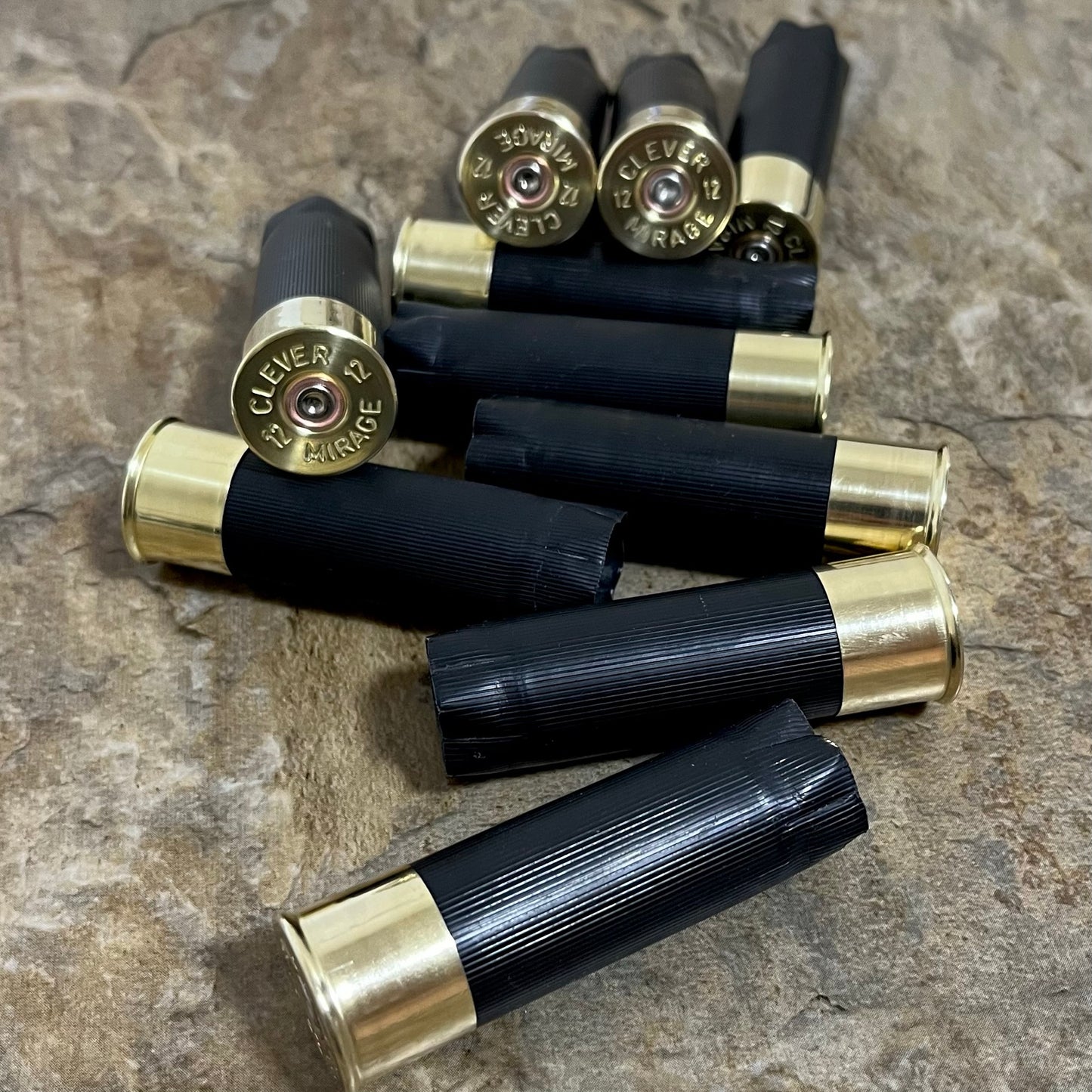 Black 12-gauge unmarked shotshells stamped Clever Mirage, scattered across a stone surface with headstamps visible for boutonnieres.