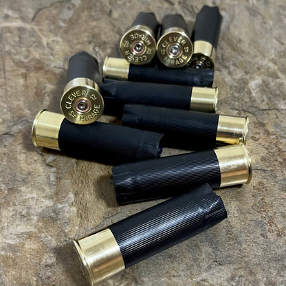 Black 12-gauge unmarked shotshells stamped Clever Mirage, scattered across a stone surface with headstamps visible for boutonnieres.