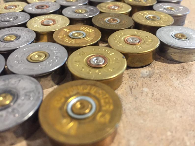A close-up angled view of gold and silver-toned 12 gauge shotgun shell headstamps on a textured surface.
