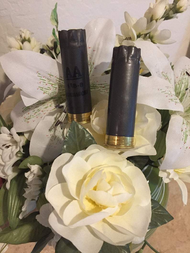 Two dark gray Winchester AA hulls with brass bases nestled inside a white and green floral boutonniere arrangement.
