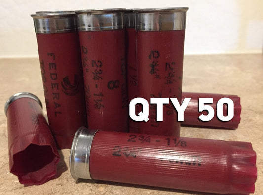 Four standing and two lying dark red 12 gauge shotgun hulls with silver bases and white text reading QTY 50.