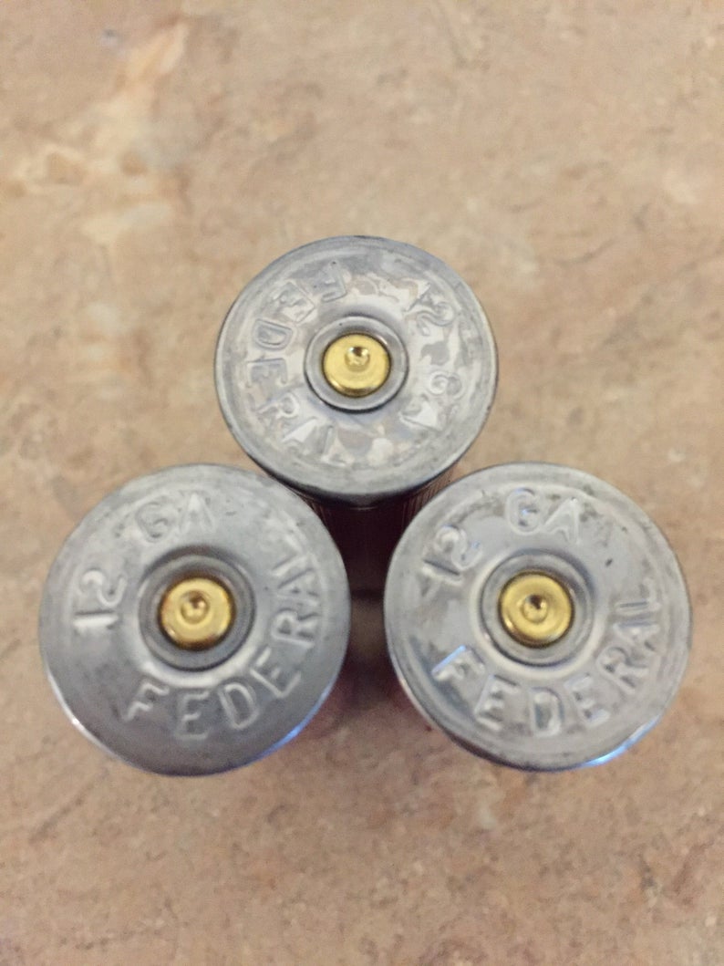 A close-up of the silver bases on three authentic, once-fired dark red Federal 12-gauge empty shotgun shells. These recovered casings show clear headstamps, perfect for high-quality rustic DIY crafting projects.