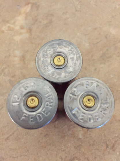 A close-up of the silver bases on three authentic, once-fired dark red Federal 12-gauge empty shotgun shells. These recovered casings show clear headstamps, perfect for high-quality rustic DIY crafting projects.