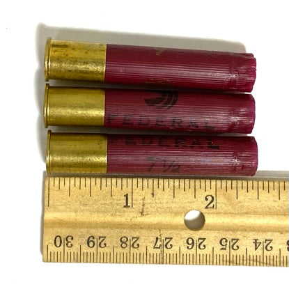 Three dark red Federal 410 bore empty shotgun shells laid next to a wooden ruler showing a length of about 2 inches