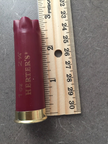 Single burgundy Herter’s 12 gauge shotgun shell measured against a ruler, showing a length of about 2.75 inches