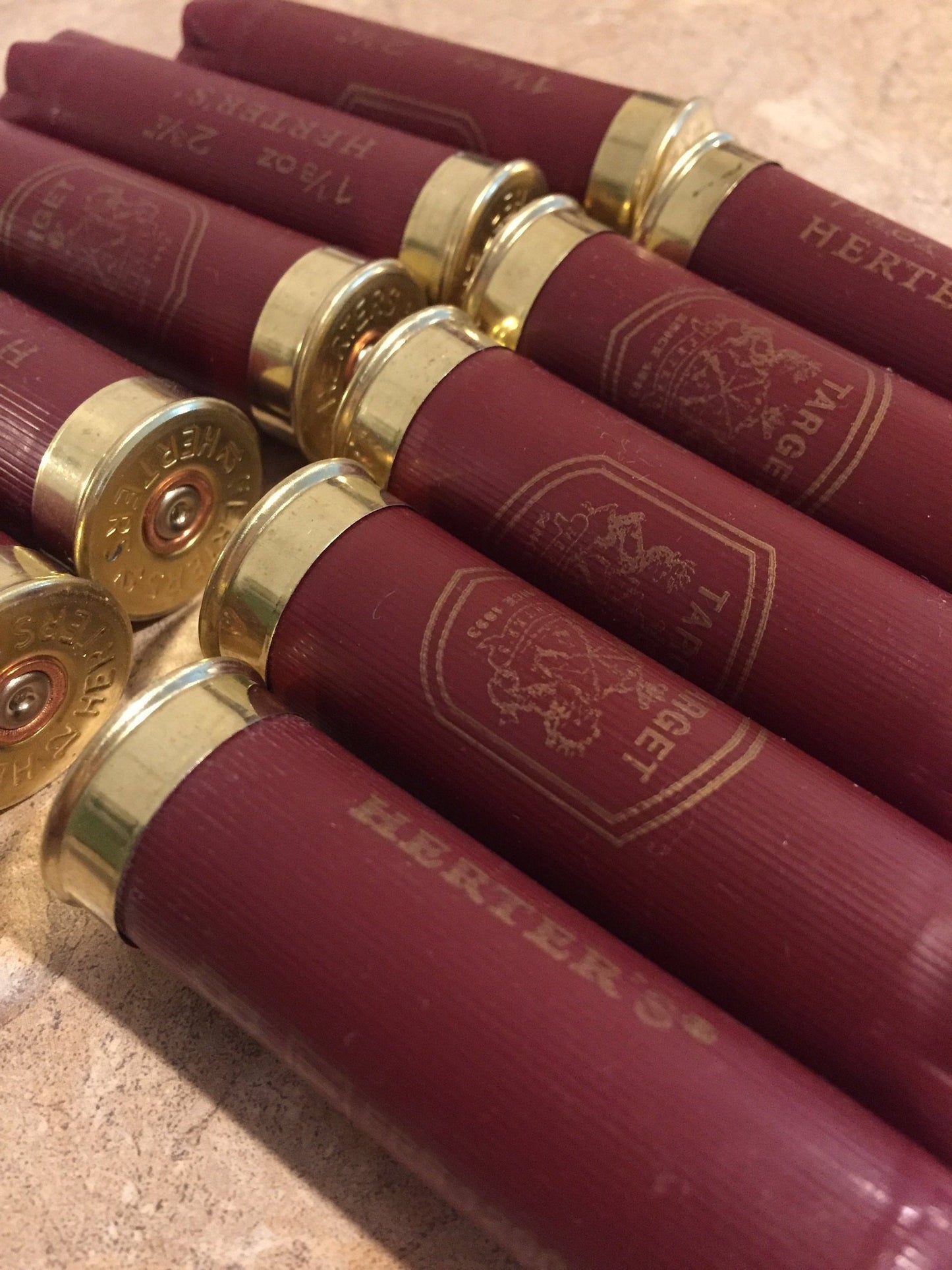 Row of burgundy Herter’s Target 12 gauge shotgun shells lying on a stone countertop, showing gold star-crimped tops and bases