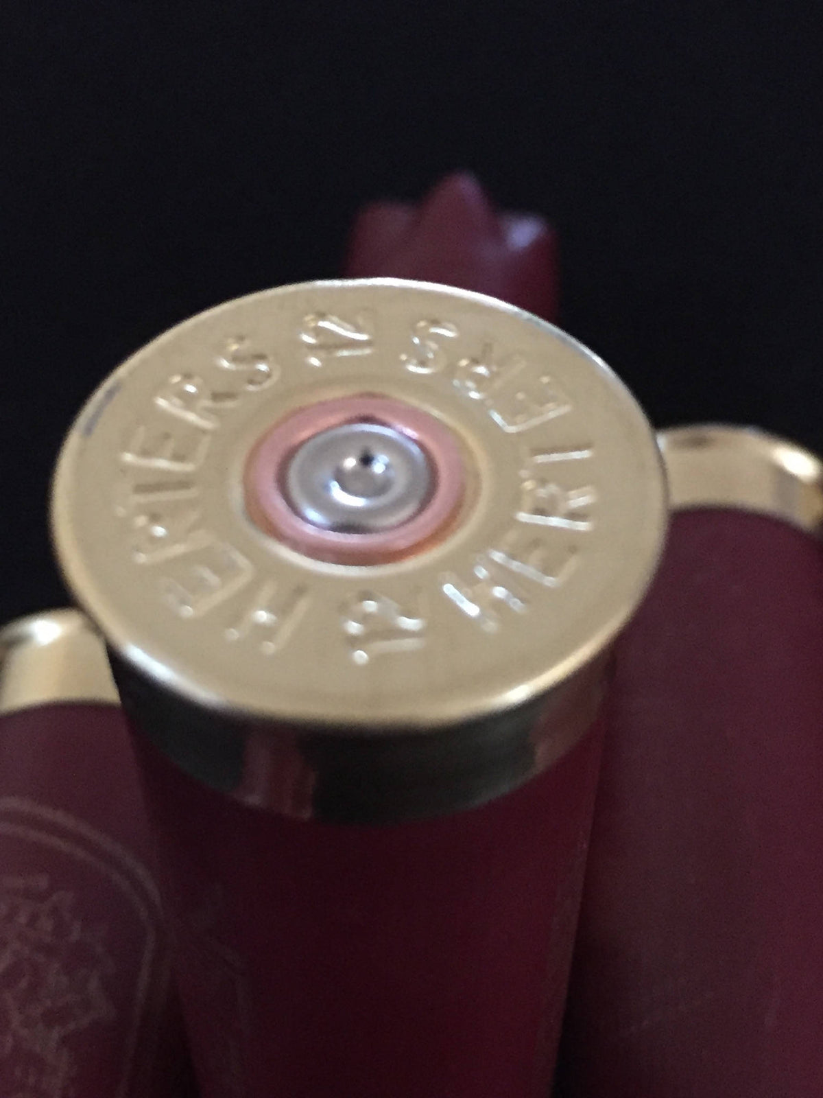 Closeup of a gold Herter’s 12 gauge shotgun shell base stamped ‘Herters 12’ beside burgundy hulls
