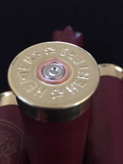 Closeup of a gold Herter’s 12 gauge shotgun shell base stamped ‘Herters 12’ beside burgundy hulls