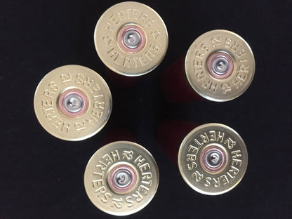 Five gold Herter’s 12 gauge shotgun shell bases arranged in a circular pattern, viewed from above on a black background