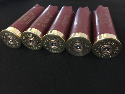 Five gold Herter’s 12 gauge shotgun shell bases viewed at an angle on a black background, showing burgundy hulls and stamped ‘Herters 12’ markings