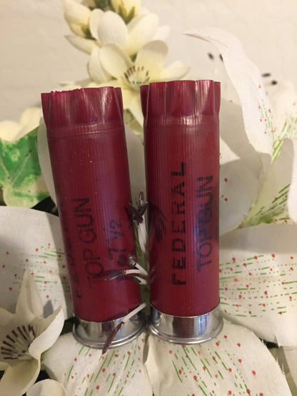 Two dark red 12 gauge shotshells with Federal Top Gun text standing vertically next to a white flower.