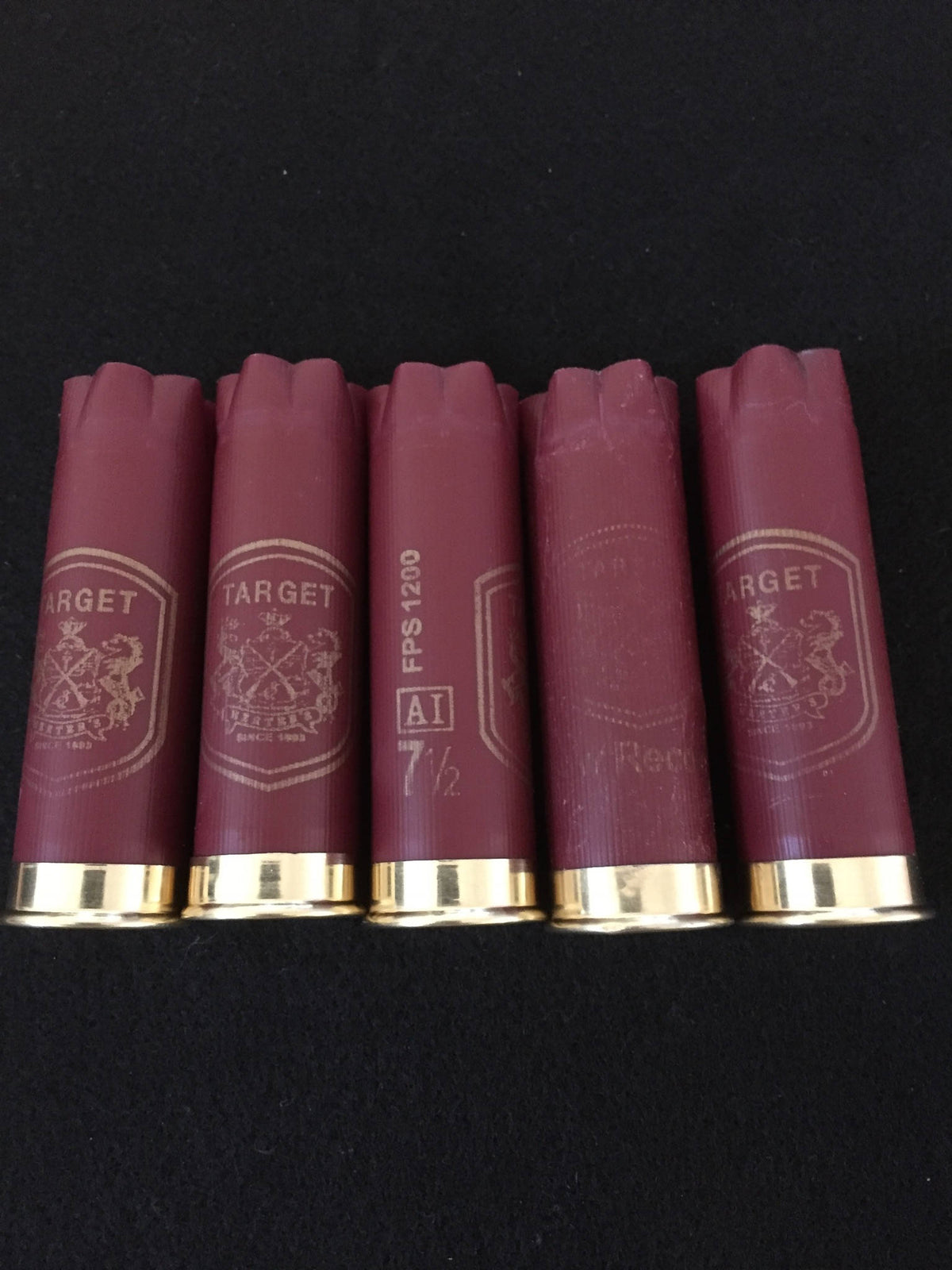 Five burgundy Herter’s Target 12 gauge shotgun shells standing upright on a black background, showing gold star-crimped tops and printed Target crest markings