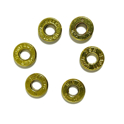 Six 9mm brass slices with primers removed arranged loosely in a ring, each stamped differently.