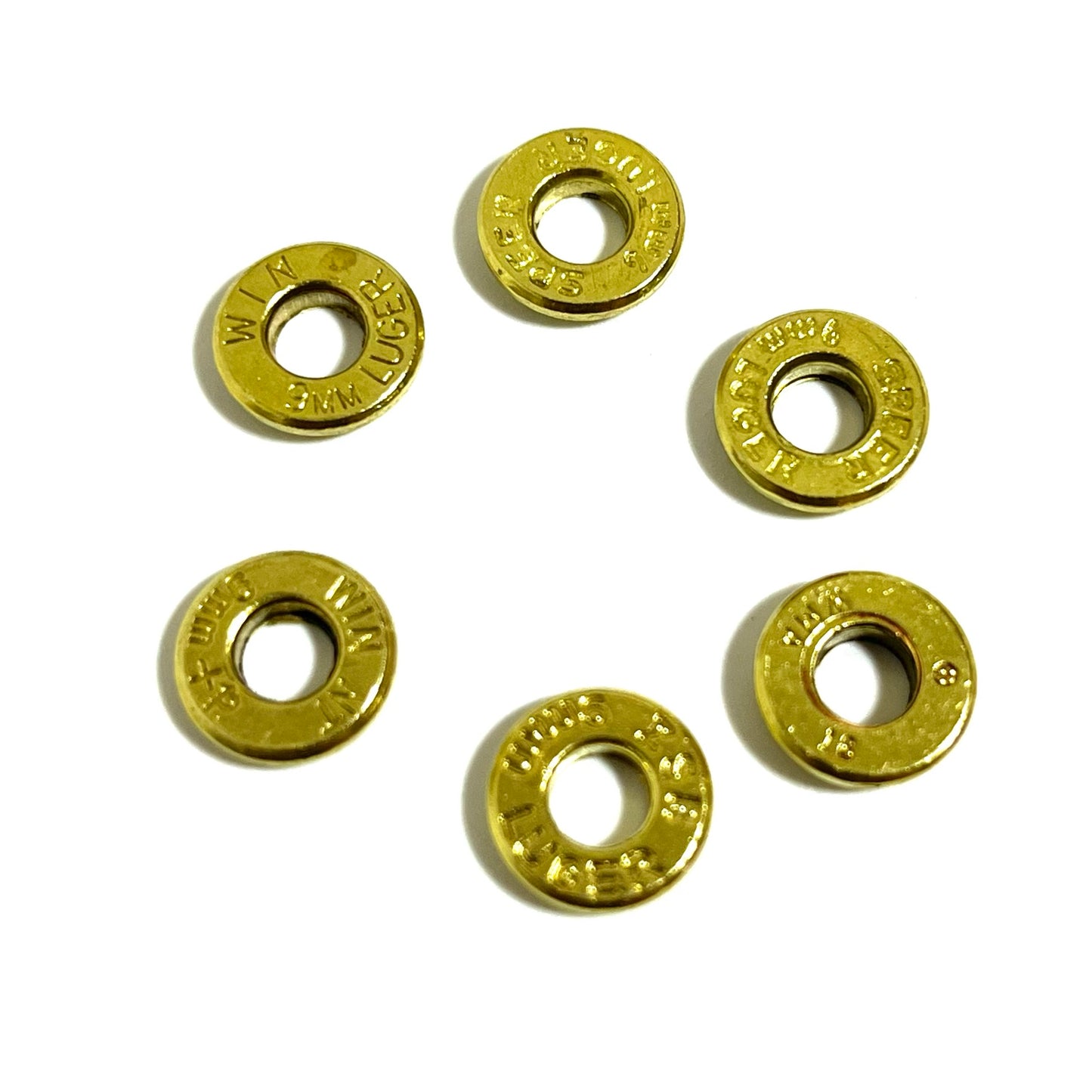 Six brass bullet slices with hollow centers arranged in a circular pattern on a white background, each stamped differently.