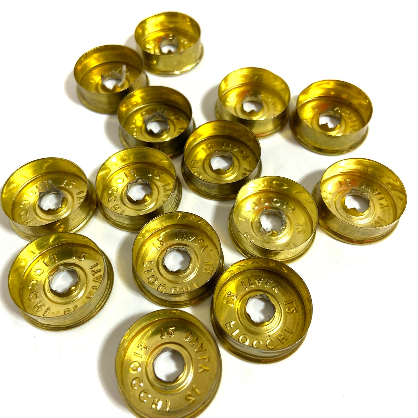 Over a dozen deprimed  gold Fiocchi 12 gauge headstamps scattered on a white background, showing headstamps.