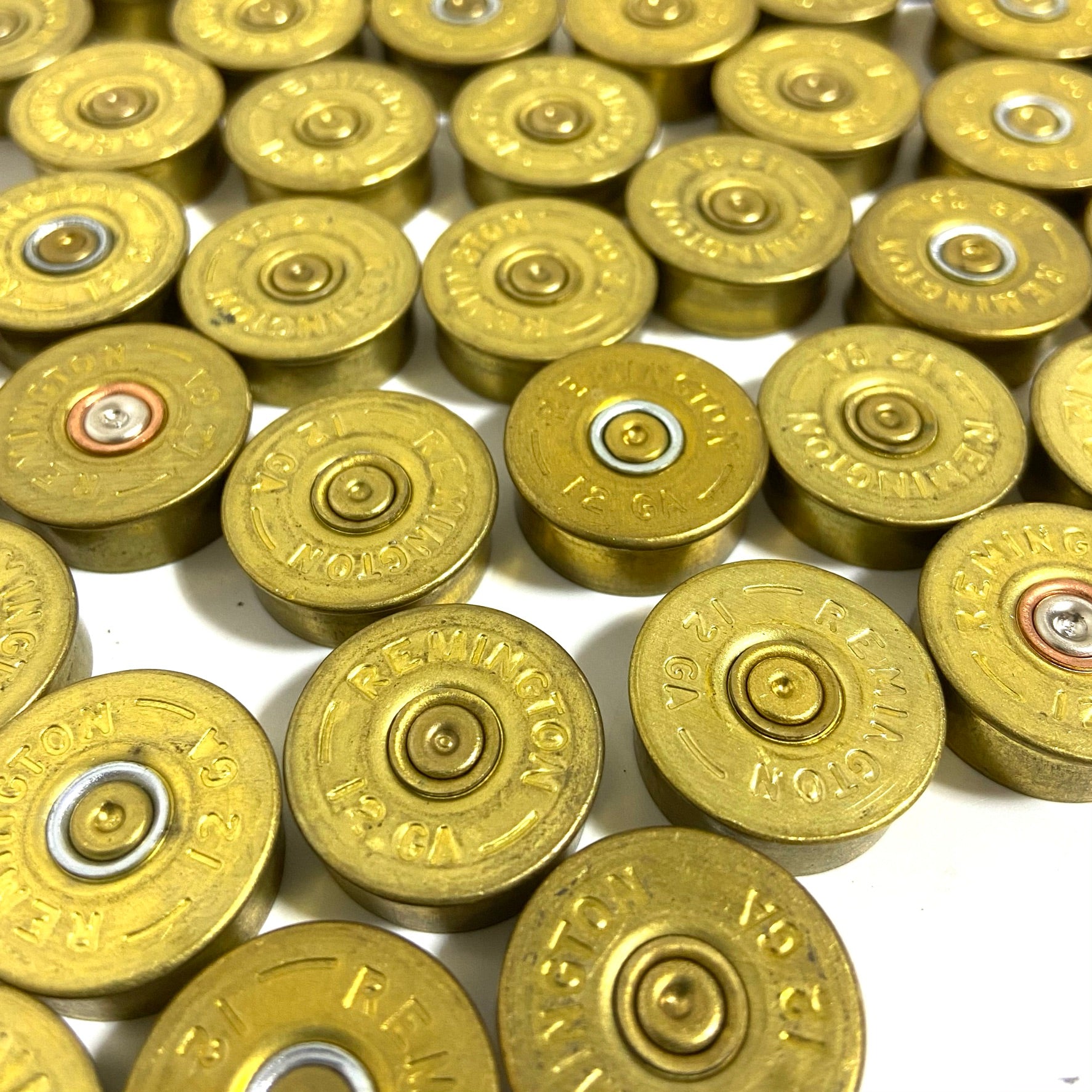 Overhead close-up of dirty unpolished 12 gauge brass end caps spread on white surface displaying stamped Remington lettering.