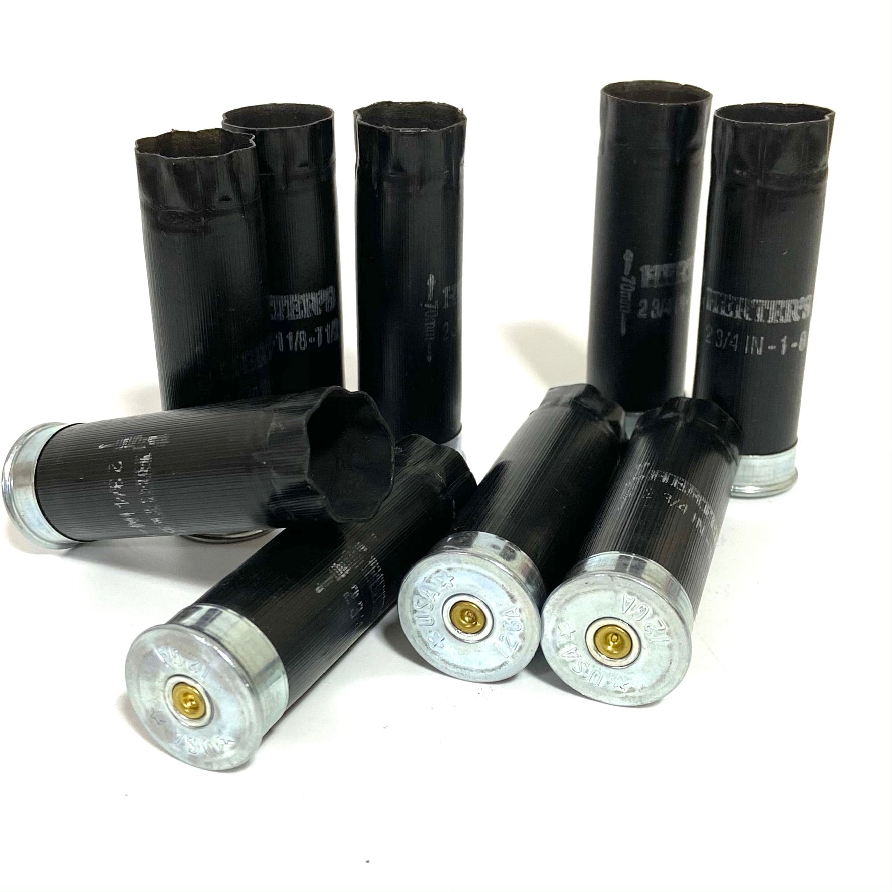Seven black Herters 12 gauge shotgun shells with silver bases standing and lying on white background