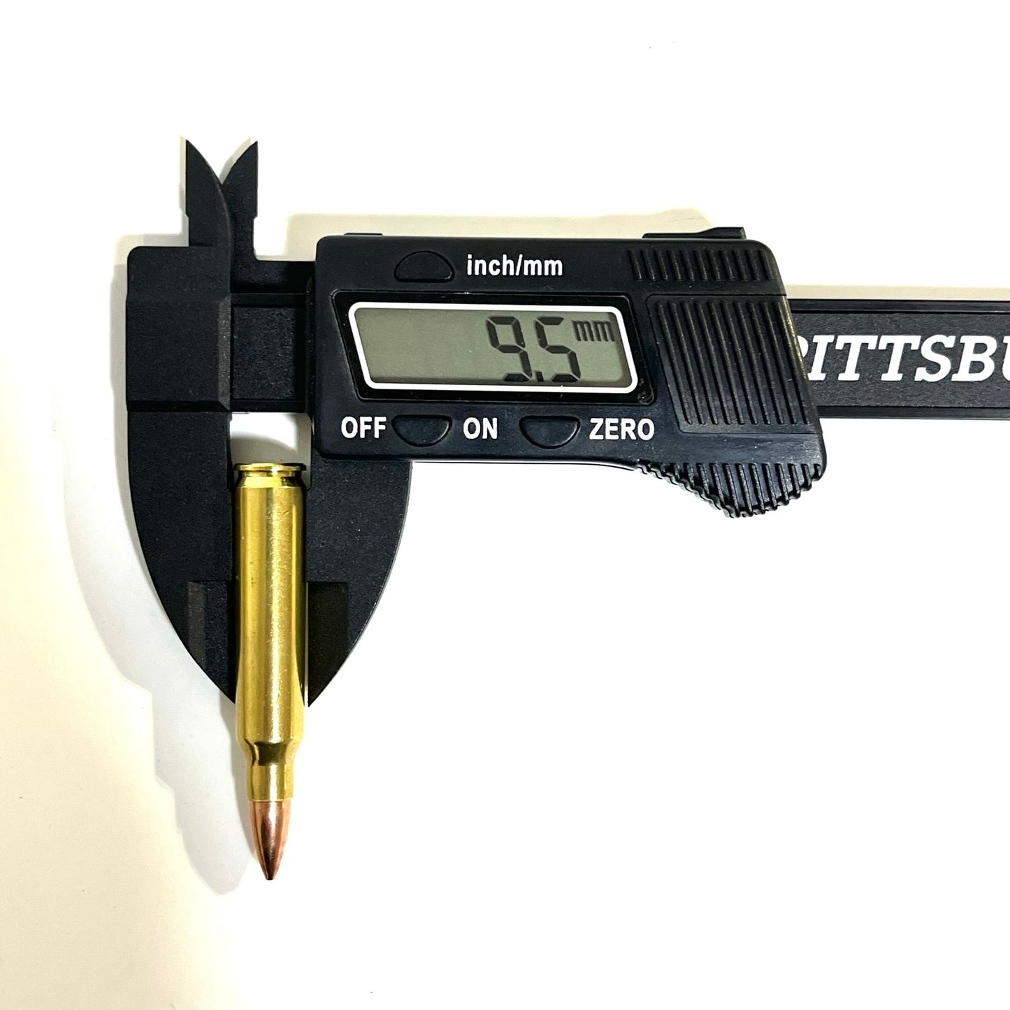 A black digital caliper measuring the diameter near the base of a single brass dummy round, displaying a reading of 9.5 mm.