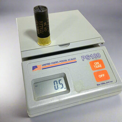 A single black shotgun shell standing upright on a digital scale displaying a weight of 0.5 ounces.