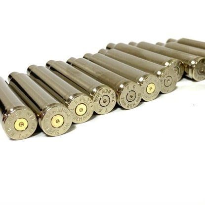 A neat row of empty 7mm nickel rifle cartridges showing the headstamps clearly on a white background.
