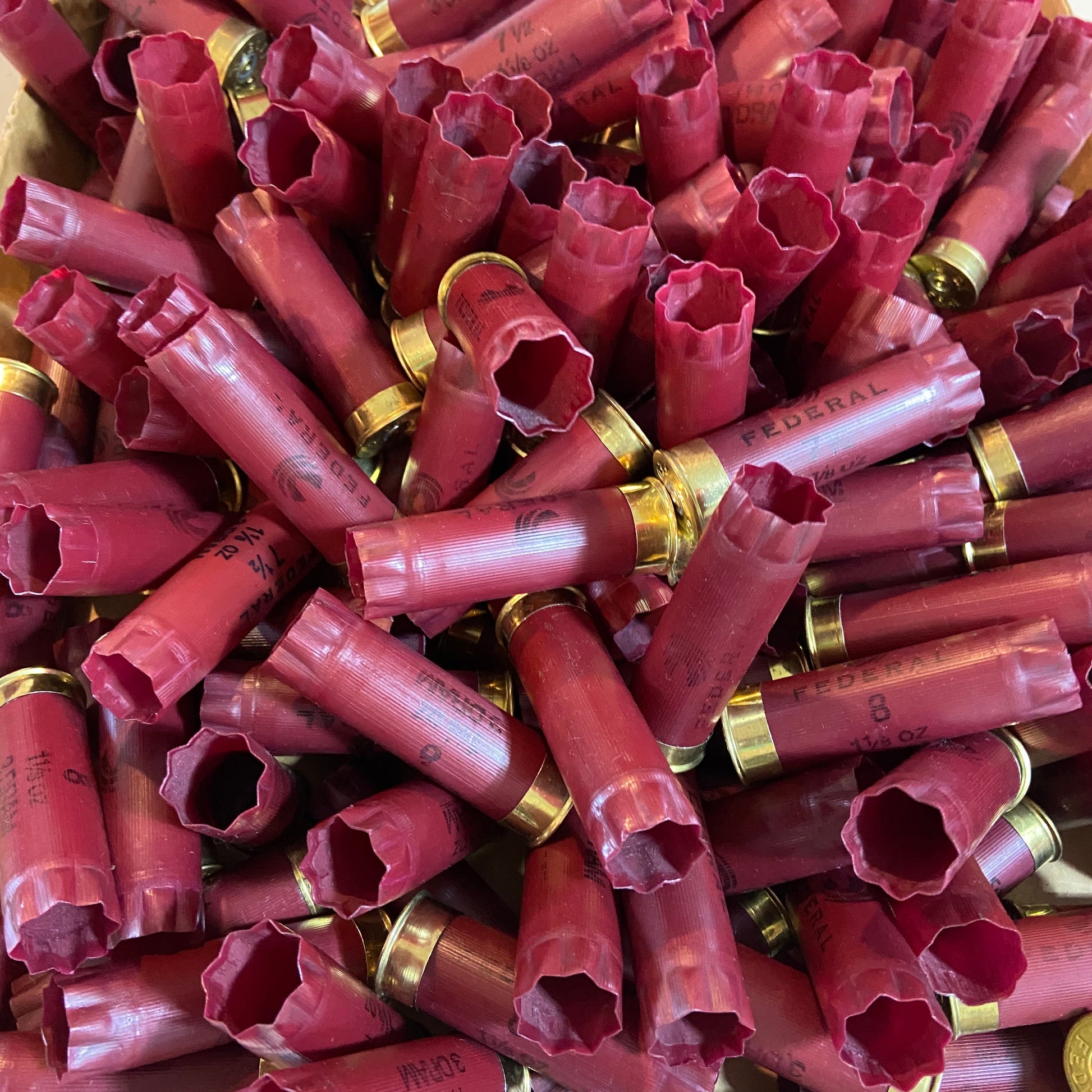 A large heap of empty burgundy shotshells with brass bases piled together in bulk.