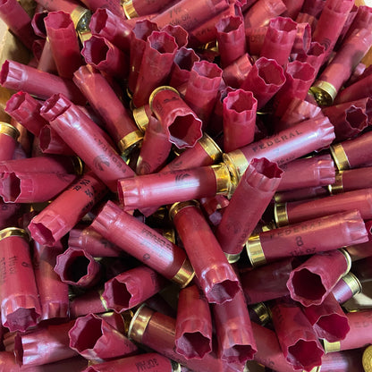 A large heap of empty burgundy shotshells with brass bases piled together in bulk.