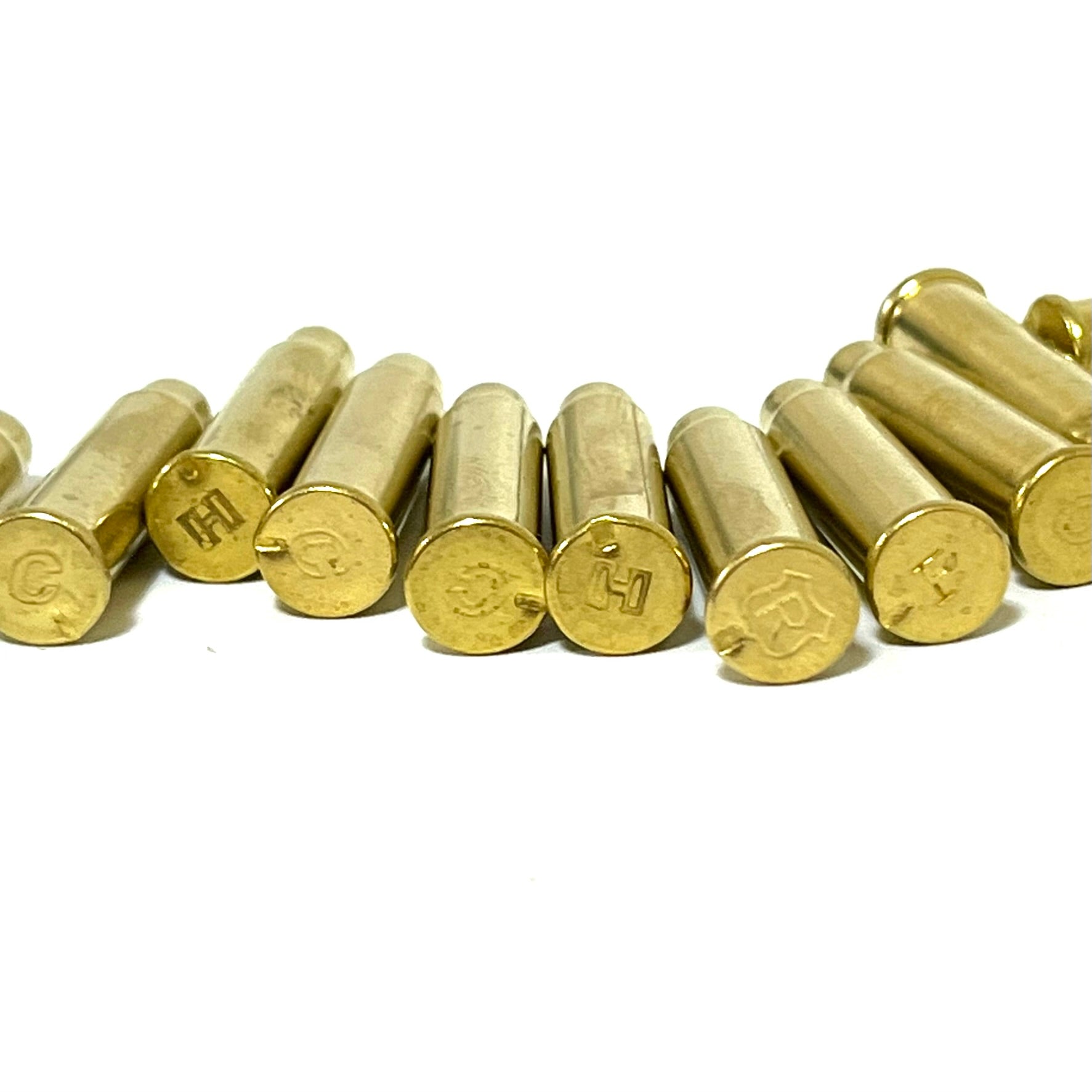 Close-up of empty brass cartridge cases with visible headstamps including letters H, C, and R on a white background.